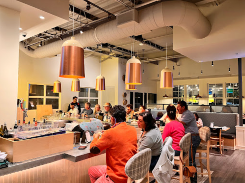 A modern restaurant interior with patrons seated at a bar, warm lighting, and a cozy atmosphere.